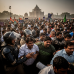 Delhi Police detaining protesters from the Cockroach Janta Party at Jantar Mantar amidst banners and placards.