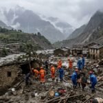 A bird's eye view of a flooded mountain valley in Nepal with destroyed houses and rescue teams working in the mud.