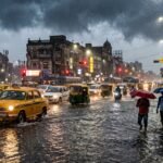 A flooded street in an Indian city during a heavy monsoon downpour with cars partially submerged.