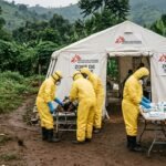 Health workers in yellow protective gear standing near a medical tent in a rural Congolese village during the Ebola crisis.