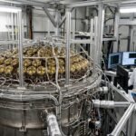 An interior view of the LUX-ZEPLIN dark matter detector featuring golden photomultiplier tubes and high-tech titanium housing in an underground laboratory.