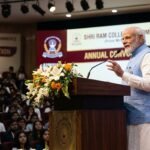 Prime Minister Narendra Modi addressing a large gathering of students at SRCC, gesturing during a speech about India's growth and optimism.