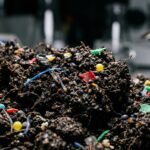 Microscopic view of soil particles contaminated with synthetic microplastic fibers and chemical pollutants.