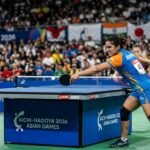 An intense moment from the 2026 Asian Games table tennis match where an Indian female athlete executes a powerful backhand stroke against Singapore.