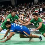 A high-action moment from the 2026 Asian Games Kabaddi final where a raider in a blue jersey attempts a leap over a defensive chain.