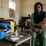 A close-up of a healthcare professional in Pakistan holding a pediatric HIV diagnostic kit in a clinical setting.