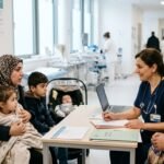 A healthcare professional discusses a medical report with a patient in a modern clinical setting, representing the intersection of migration and public health services.