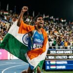 Indian athlete celebrating with the national flag at the 2026 Asian Games stadium.