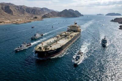 A military patrol boat guarding the narrow shipping lanes of the Strait of Hormuz with an oil tanker in the background.