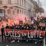 French students holding banners and flares during a large-scale protest in front of a closed Parisian school building.