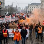 A large crowd of protesters in a European city holding banners and flares during a demonstration against inflation and high energy costs.