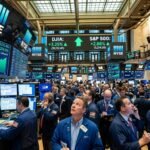 Traders on the floor of the New York Stock Exchange looking at large green digital displays showing the market recovery.