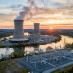 A modern nuclear power plant facility with steam rising from cooling towers under a bright blue sky, symbolizing clean energy growth.